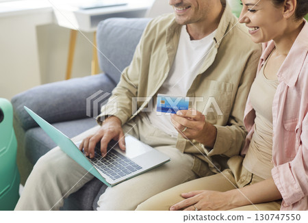 Happy couple booking vacation online with laptop and credit card at cozy home 130747550