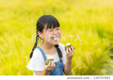 A girl eating rice balls in front of a rice field A girl eating rice balls in front of a rice field 130747905
