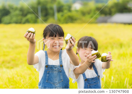 Sisters holding rice balls in front of a rice field Sisters holding rice balls in front of a rice field 130747908
