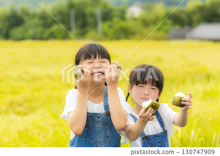 Sisters holding rice balls in front of a rice field Sisters holding rice balls in front of a rice field 130747909