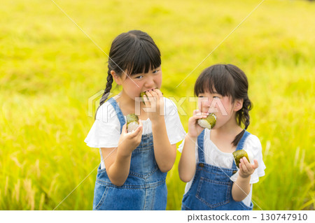 Sisters holding rice balls in front of a rice field Sisters holding rice balls in front of a rice field 130747910