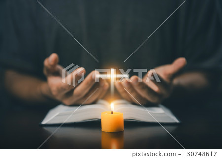 Christian man worship. Hands folded in prayer on a Holy Bible in home concept for faith. Spirituality and religion. Man praying on holy bible with candle light. Man hand with Bible praying. Christian man worship. Hands folded in prayer on a Holy Bible in home concept for faith. Spirituality and religion. Man praying on holy bible with candle light. Man hand with Bible praying. 130748617