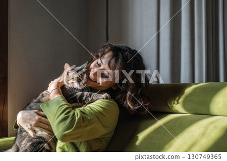 Woman Hugging Cat on Green Couch in Morning Light. 130749365
