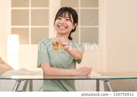 A young Asian woman having a drink in her bedroom at home (drinking at home, tipsy, drinking at home, drinking) 130750912