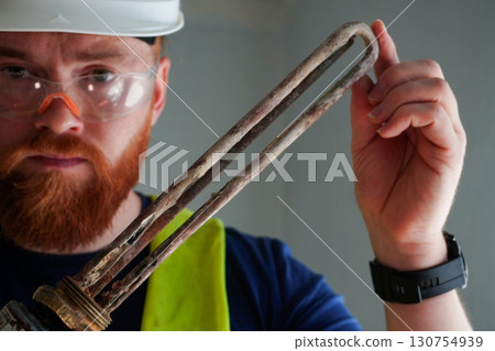 Water heating technician demonstrating scale-damaged heating element 130754939