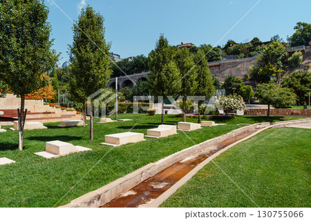 Sunlit park scene showcasing greenery and walking paths in a serene outdoor space with trees and landscaping Sunlit park scene showcasing greenery and walking paths in a serene outdoor space with trees and landscaping 130755066