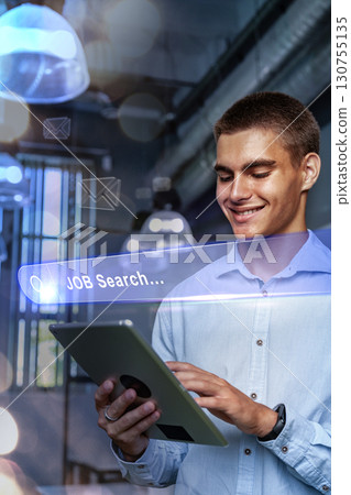 Young professional engaged in a job search while using a tablet in a modern workspace during evening hours 130755135