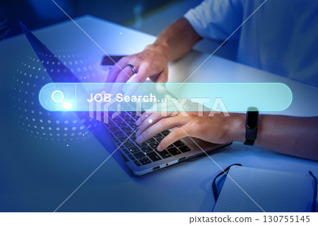 Individual using a laptop for job search in a modern, well-lit workspace during the evening 130755145