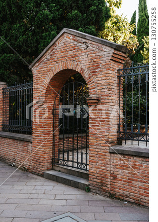 Historic brick archway with wrought iron gate in urban garden during sunset 130755258