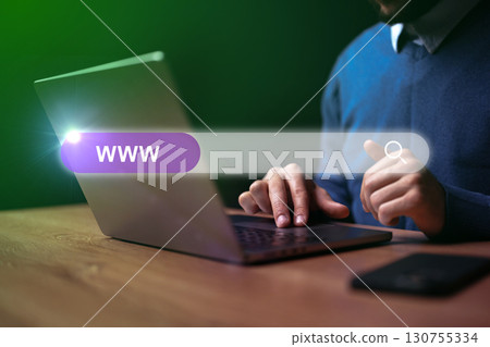 Man browsing the internet on laptop in an indoor setting during evening hours with a focus on search bar 130755334