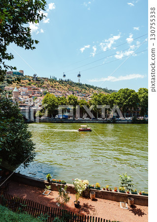 Beautiful riverside view in Tbilisi with greenery, buildings, and cable cars against a clear sky Beautiful riverside view in Tbilisi with greenery, buildings, and cable cars against a clear sky 130755338