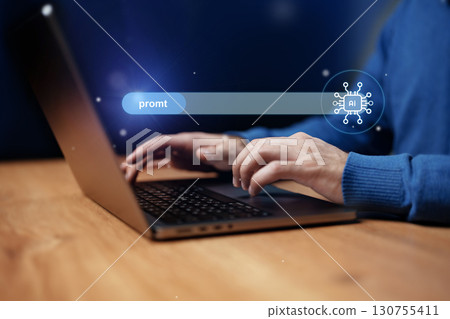 Individual typing on a laptop with AI prompt search bar illuminated in a dimly lit workspace setting at night 130755411