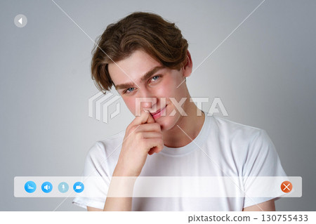 Young man smiles playfully while resting his chin on his hand against a neutral background Young man smiles playfully while resting his chin on his hand against a neutral background 130755433