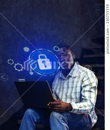 Young man working on cybersecurity project while seated with laptop in a dimly lit space 130755559