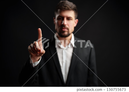 Business professional in formal attire signaling a message with a raised finger in a dark setting Business professional in formal attire signaling a message with a raised finger in a dark setting 130755673