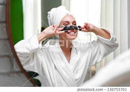 Woman enjoying a skincare routine while smiling in a bright, modern bathroom in the morning 130755701