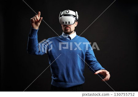Man engages in virtual reality experience while wearing a headset in a dark studio setting 130755752