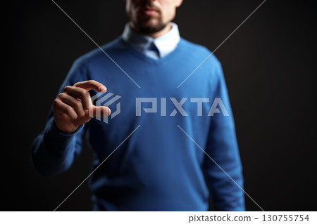 Person in blue sweater using hand gesture to symbolize measurement against dark background Person in blue sweater using hand gesture to symbolize measurement against dark background 130755754