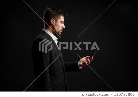 Professional man in formal attire looking at smartphone in dark environment during evening hours Professional man in formal attire looking at smartphone in dark environment during evening hours 130755802