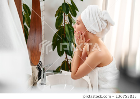 Woman applying facial skincare in a serene bathroom with plants and natural light in the early morning 130755813