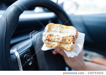 Asian woman driver hold and eat hamburger in car, dangerous and risk an accident. Asian woman driver hold and eat hamburger in car, dangerous and risk an accident. 130755835