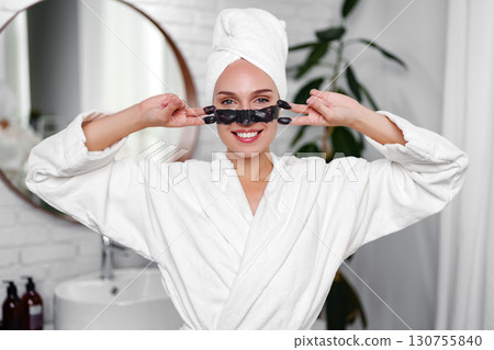 Woman applying facial mask in spa bathroom while wearing a bathrobe and towel, enjoying a self-care moment Woman applying facial mask in spa bathroom while wearing a bathrobe and towel, enjoying a self-care moment 130755840