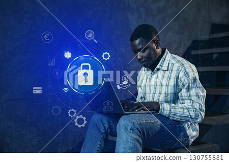 Man using laptop on stairs with digital security icons in a modern workspace during evening hours Man using laptop on stairs with digital security icons in a modern workspace during evening hours 130755881