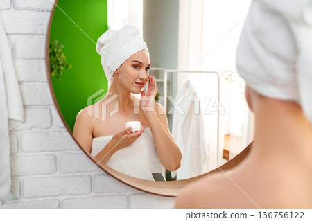 Woman applying skincare in modern bathroom with green accents during morning routine 130756122