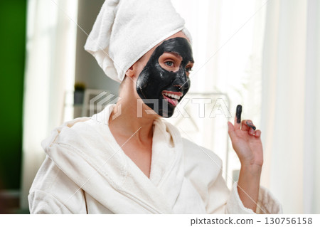 Woman enjoying a facial mask treatment at a spa while wearing a bathrobe and towel in a bright room during daytime Woman enjoying a facial mask treatment at a spa while wearing a bathrobe and towel in a bright room during daytime 130756158