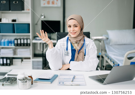 Beautiful physician doctor sit on table in office hospital. Attractive therapist female practitioner pharmacist smile and use tablet and laptop. Beautiful physician doctor sit on table in office hospital. Attractive therapist female practitioner pharmacist smile and use tablet and laptop. 130756253