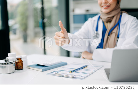 Beautiful physician doctor sit on table in office hospital. Attractive therapist female practitioner pharmacist smile and use tablet and laptop. 130756255