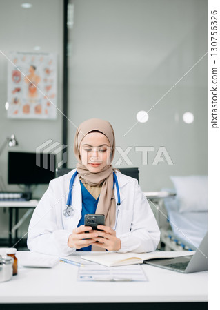 Beautiful physician doctor sit on table in office hospital. Attractive therapist female practitioner pharmacist smile and use tablet and laptop. Beautiful physician doctor sit on table in office hospital. Attractive therapist female practitioner pharmacist smile and use tablet and laptop. 130756326
