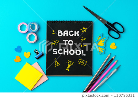 Colorful school supplies on a bright blue background with a notebook inviting students back to school 130756331