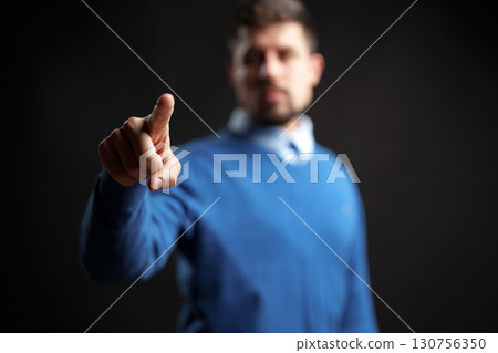Person in blue sweater pointing with finger in dramatic lighting against black background Person in blue sweater pointing with finger in dramatic lighting against black background 130756350
