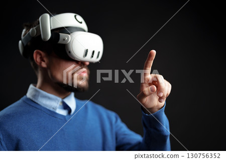 Man wearing virtual reality headset interacts with digital environment in a dark setting during an immersive gaming experience Man wearing virtual reality headset interacts with digital environment in a dark setting during an immersive gaming experience 130756352