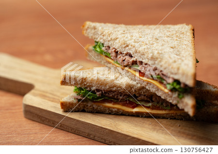 Delicious whole grain sandwich with layers of tuna, lettuce, and cheese served on a wooden cutting board at lunchtime Delicious whole grain sandwich with layers of tuna, lettuce, and cheese served on a wooden cutting board at lunchtime 130756427