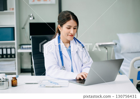Beautiful physician doctor sit on table in office hospital. Attractive therapist female practitioner pharmacist smile and use tablet and laptop. Beautiful physician doctor sit on table in office hospital. Attractive therapist female practitioner pharmacist smile and use tablet and laptop. 130756431