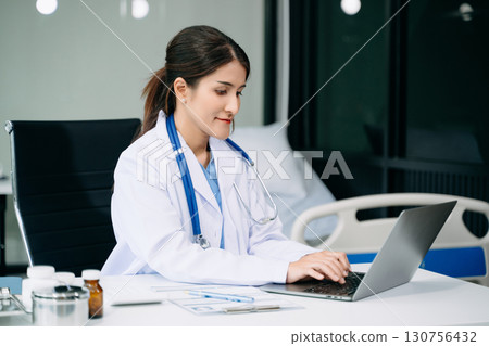 Beautiful physician doctor sit on table in office hospital. Attractive therapist female practitioner pharmacist smile and use tablet and laptop. Beautiful physician doctor sit on table in office hospital. Attractive therapist female practitioner pharmacist smile and use tablet and laptop. 130756432