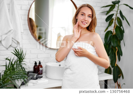 Woman applying skincare in modern bathroom with plants and natural light during morning routine 130756468