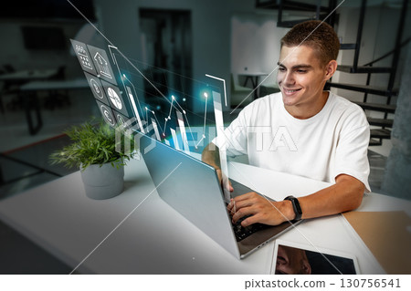 Young man analyzing data on a laptop with digital graphs in a modern workspace during daytime Young man analyzing data on a laptop with digital graphs in a modern workspace during daytime 130756541