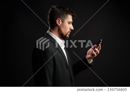 Businessman checking his smartphone while dressed in a suit against a dark background 130756605