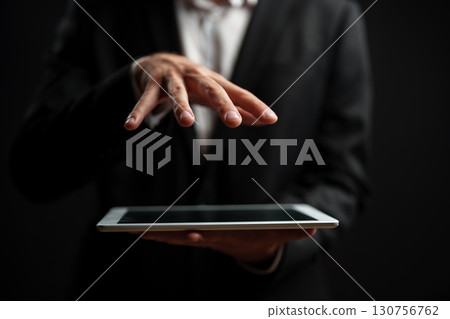 Professional man using tablet with fingers hovering over screen in dark background Professional man using tablet with fingers hovering over screen in dark background 130756762