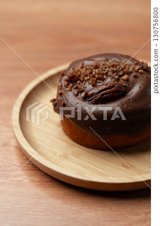 Delicious chocolate donut topped with crunchy nuts on a wooden plate in a cozy setting Delicious chocolate donut topped with crunchy nuts on a wooden plate in a cozy setting 130756800