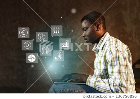 Young man using laptop with digital icons representing finance in a warm indoor setting 130756856