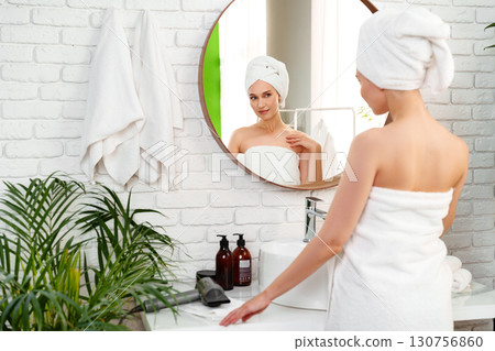 Woman preparing in a bright bathroom with a mirror and green plants after a relaxing shower Woman preparing in a bright bathroom with a mirror and green plants after a relaxing shower 130756860