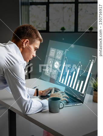 Young professional working on a laptop while analyzing financial data in a modern office setting 130756917