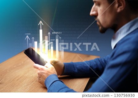 Man using smartphone for business analysis with digital data visualization in a modern workspace during daytime 130756930