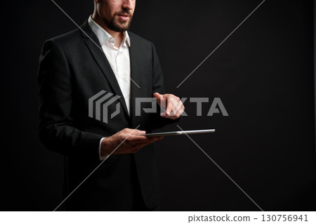 Business professional engaged in a presentation using a tablet in a dark studio setting Business professional engaged in a presentation using a tablet in a dark studio setting 130756941