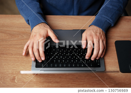 Hands typing on a sleek laptop keyboard while seated at a wooden desk in a cozy indoor workspace Hands typing on a sleek laptop keyboard while seated at a wooden desk in a cozy indoor workspace 130756989