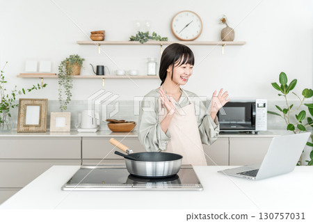 一位年輕的亞洲女性在廚房做飯時看著筆記型電腦 一位年輕的亞洲女性在廚房做飯時看著筆記型電腦 130757031
